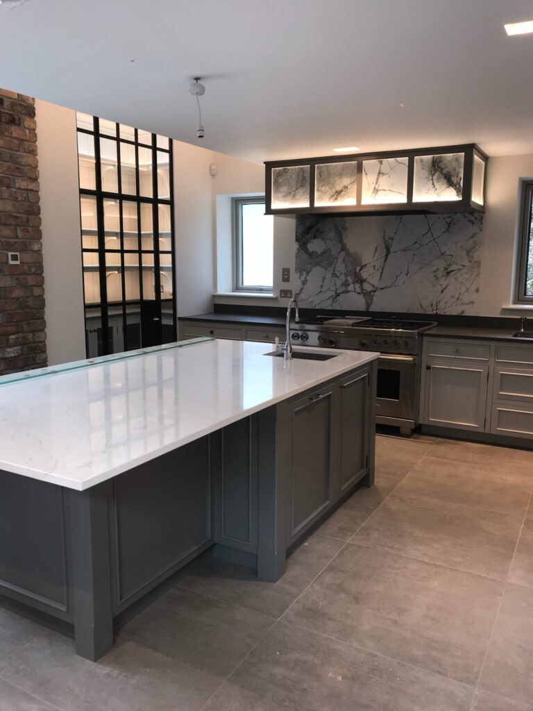 Kitchen with a large island, integral sink, range cooker and a backlit glass display cabinet above the hob