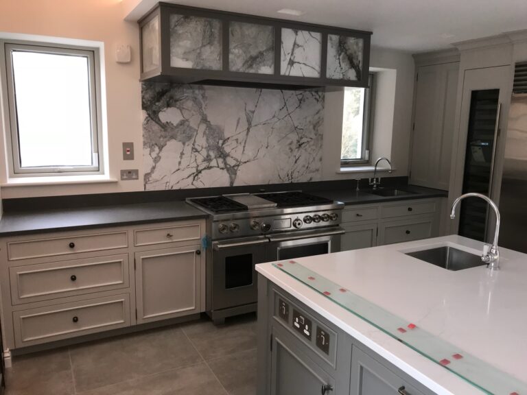 Bespoke kitchen with a range cooker set beneath a stone splashback and matching overhead cabinet, plus a central island with sink