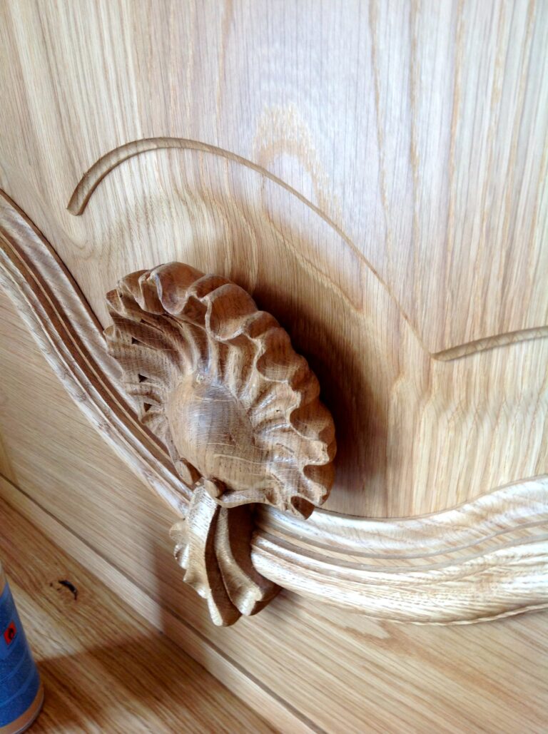 Close-up of a hand-carved timber panel featuring a decorative flower and ribbon design on a cabinet door