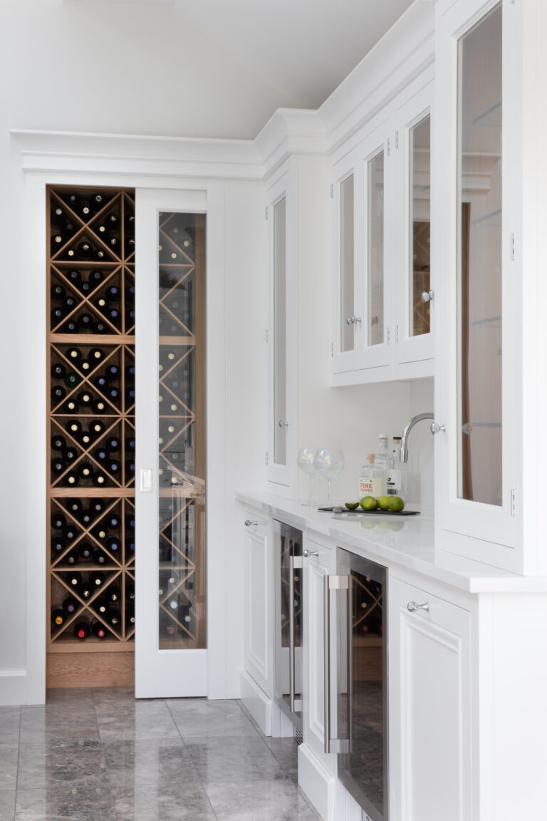 Home bar with white cabinetry, glazed display doors, wine fridges and a separate wine store with diamond bottle racking