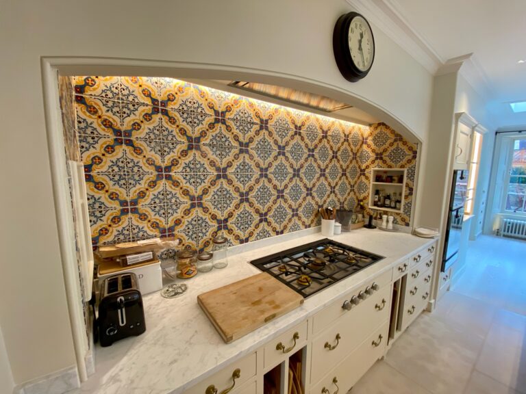 Kitchen alcove with patterned tiled splashback, gas hob set into a stone worktop, and cream cabinetry with brass handles