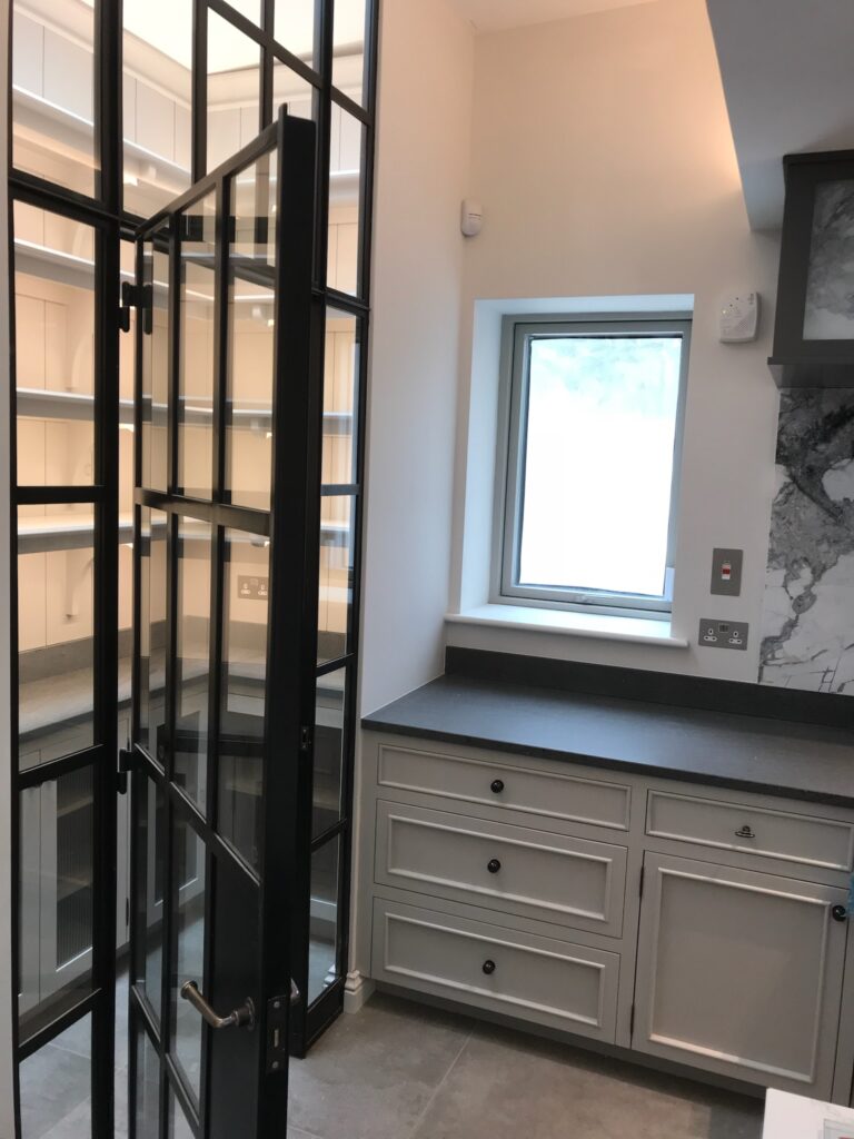 Kitchen with black-framed glazed pantry door, fitted cabinetry with dark worktop and a small window above