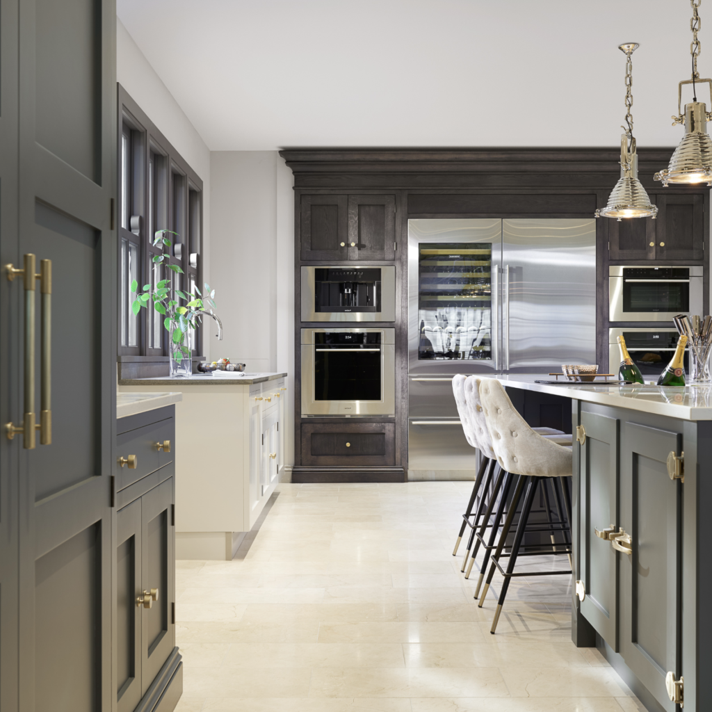 Kitchen with dark cabinetry, integrated steel appliances, stone worktops and an island with upholstered bar stools