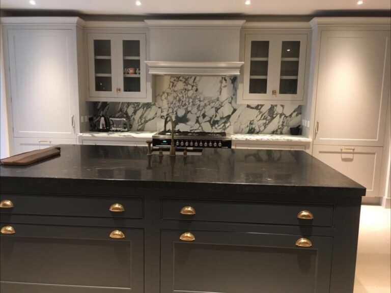 Kitchen island with dark worktop and brass cup handles, facing a gas hob set into a stone splashback