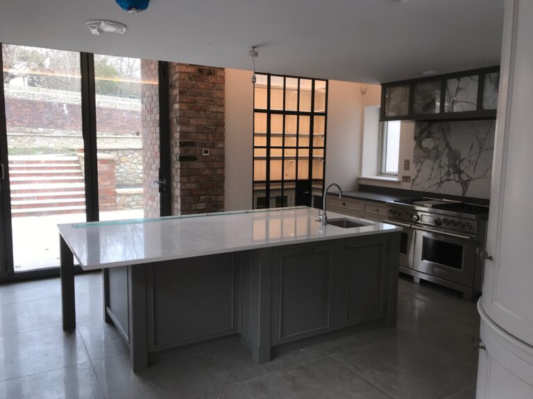 Kitchen with a large island, integrated sink, range cooker and glazed cabinetry beside an exposed brick wall