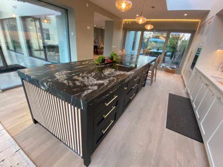 Large kitchen island with a dark veined stone worktop, slatted panel sides and brass drawer handles