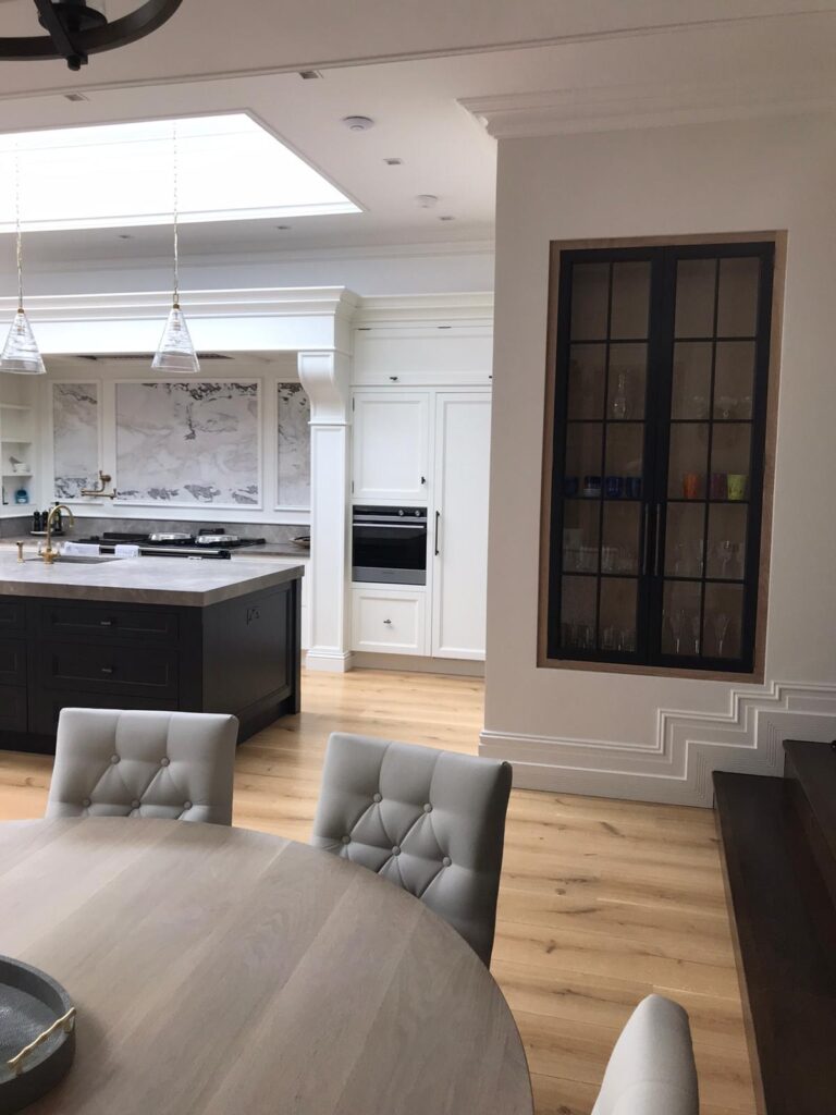 Open-plan kitchen and dining area with a dark central island, built-in glazed display cabinet and round dining table