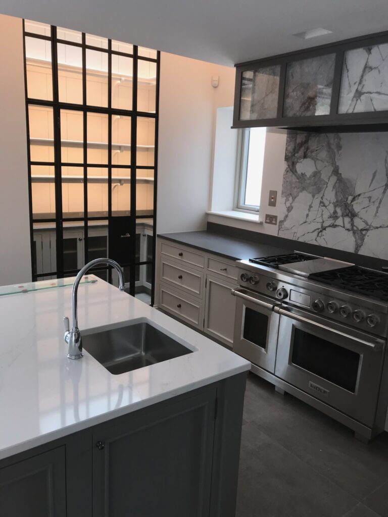 Kitchen with island sink, range cooker beneath a stone splashback, and glazed doors leading to a pantry