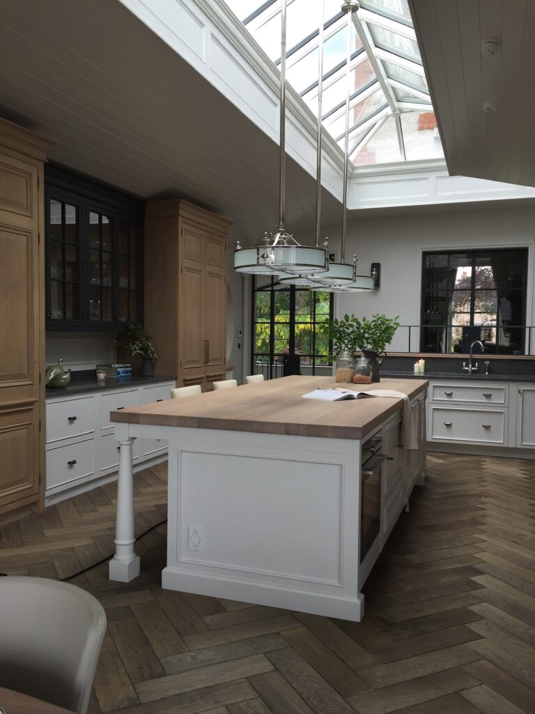 Kitchen with a large painted island, wooden worktop, herringbone flooring and a glazed roof lantern above