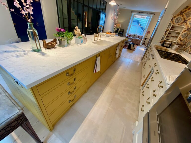 Kitchen island with yellow cabinetry, brass handles and a stone worktop, leading through to a sitting room