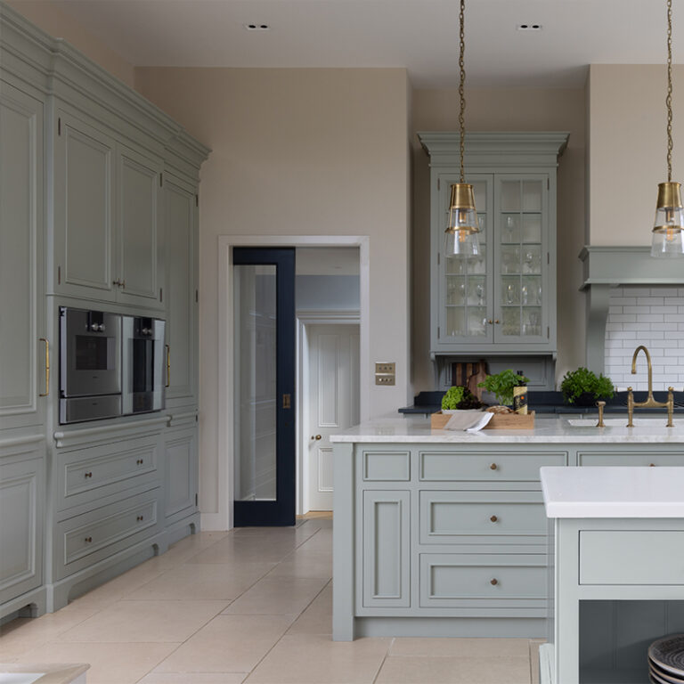 Bespoke kitchen with painted cabinetry, glass-fronted wall units, brass pendant lights and a stone-topped island