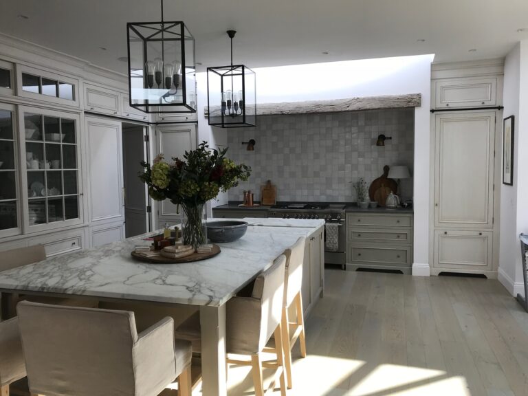 Kitchen island with stone worktop, glazed dresser, range cooker and tiled splashback beneath a reclaimed timber beam