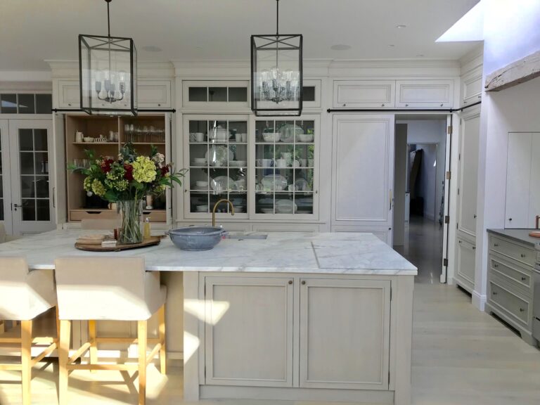 Kitchen island with stone worktop, glazed dresser units, lantern pendant lights and upholstered bar stools