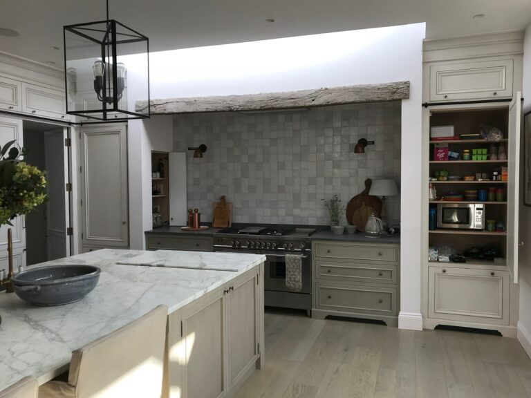 Kitchen with stone island, range cooker beneath a rustic wooden beam and tiled splashback, plus fitted pantry shelving
