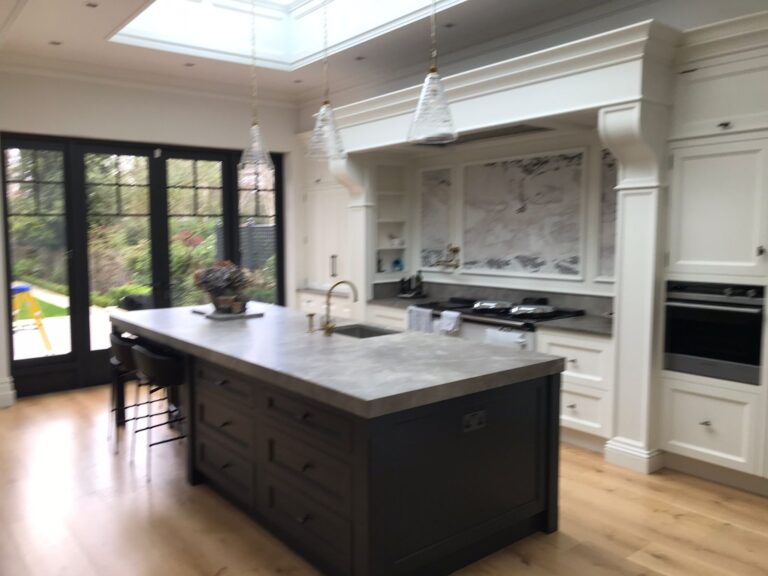 Bespoke kitchen with large island, dark cabinetry, stone-effect splashback, pendant lights and bi-fold doors to garden