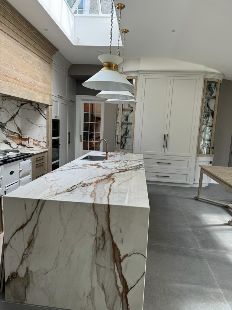 Kitchen with a large veined stone waterfall island, matching splashback, pale cabinetry and a traditional range cooker
