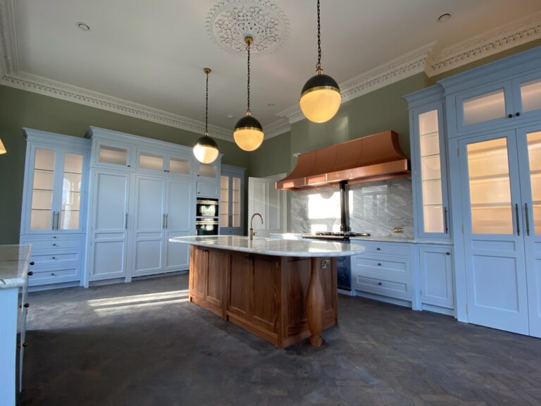 Kitchen with a timber island, stone worktop, copper extractor hood and painted glazed cabinetry around the walls