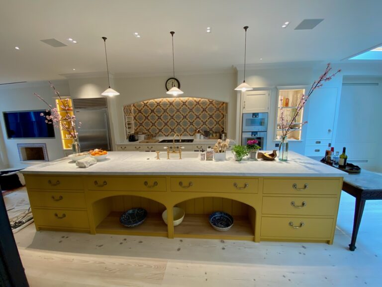 Large kitchen island with yellow cabinetry, stone worktop, brass tap, and three pendant lights above