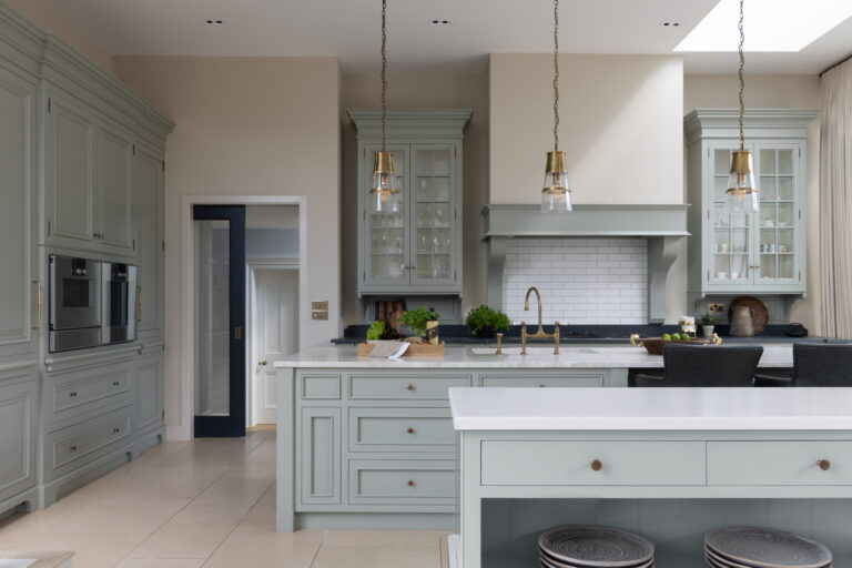 Sage Green bespoke kitchen with glazed display cabinets, brass pendant lights and a stone-topped central island