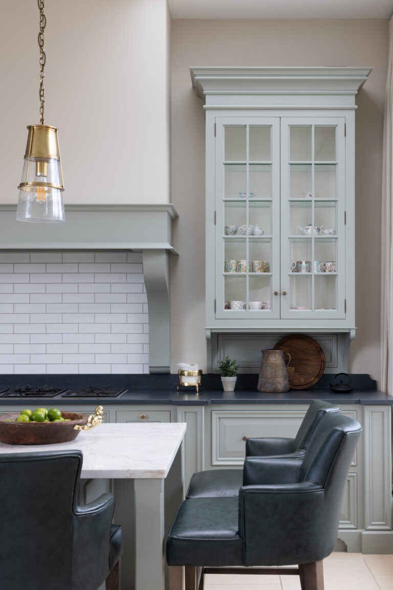 Sage green bespoke kitchen with glazed dresser cabinet, tiled splashback, dark worktops and leather bar stools