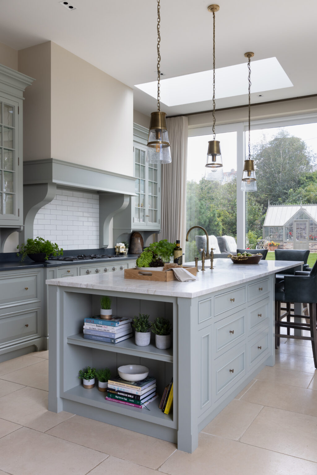 Sage Green bespoke kitchen island with stone worktop, open shelving and brass pendant lights beneath a skylight