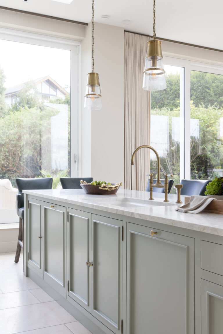 Sage Green kitchen island with stone worktop, brass tap and pendant lights beside large windows