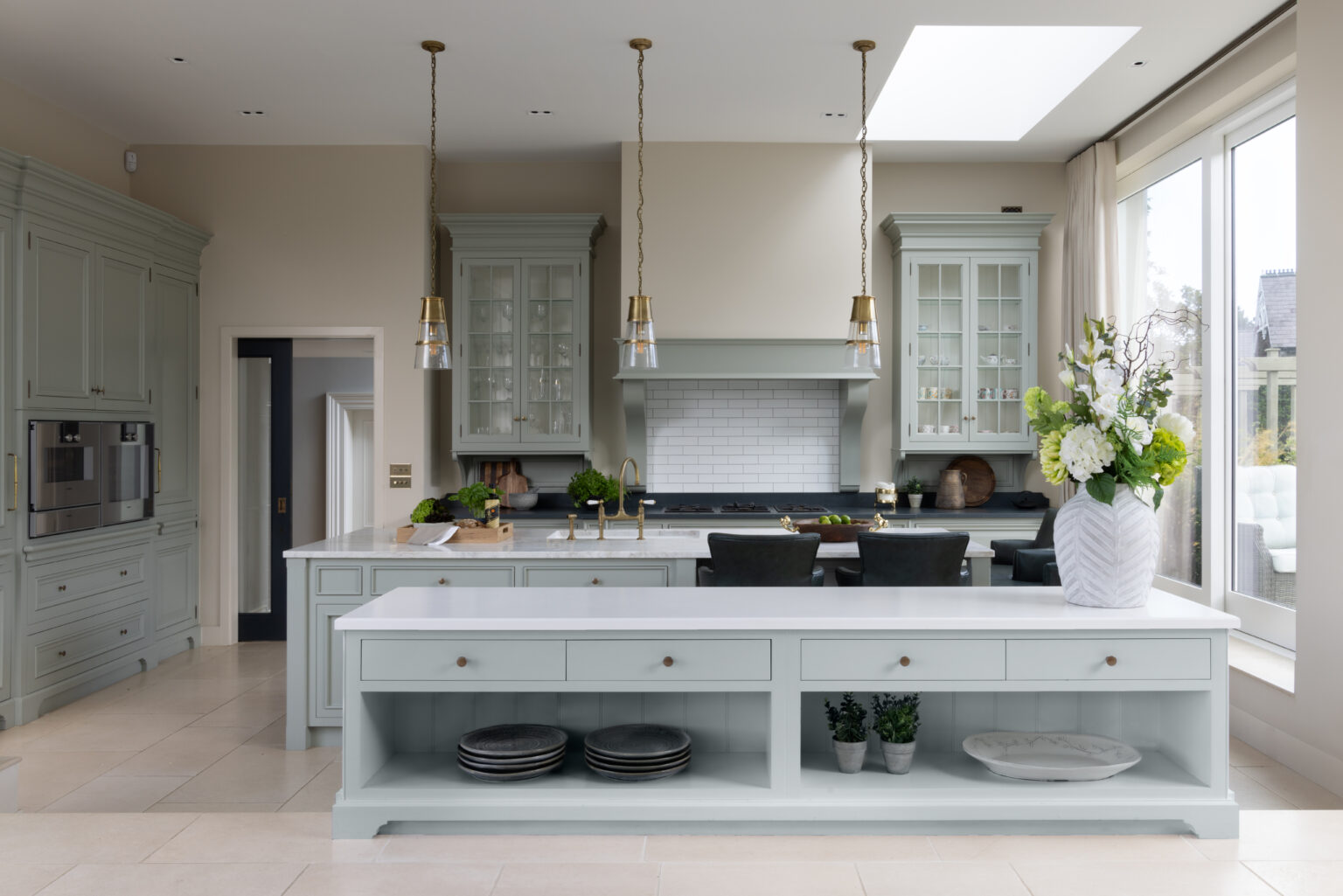 Sage Green bespoke kitchen with glazed display cabinets, brass pendant lights and an open-shelved central island