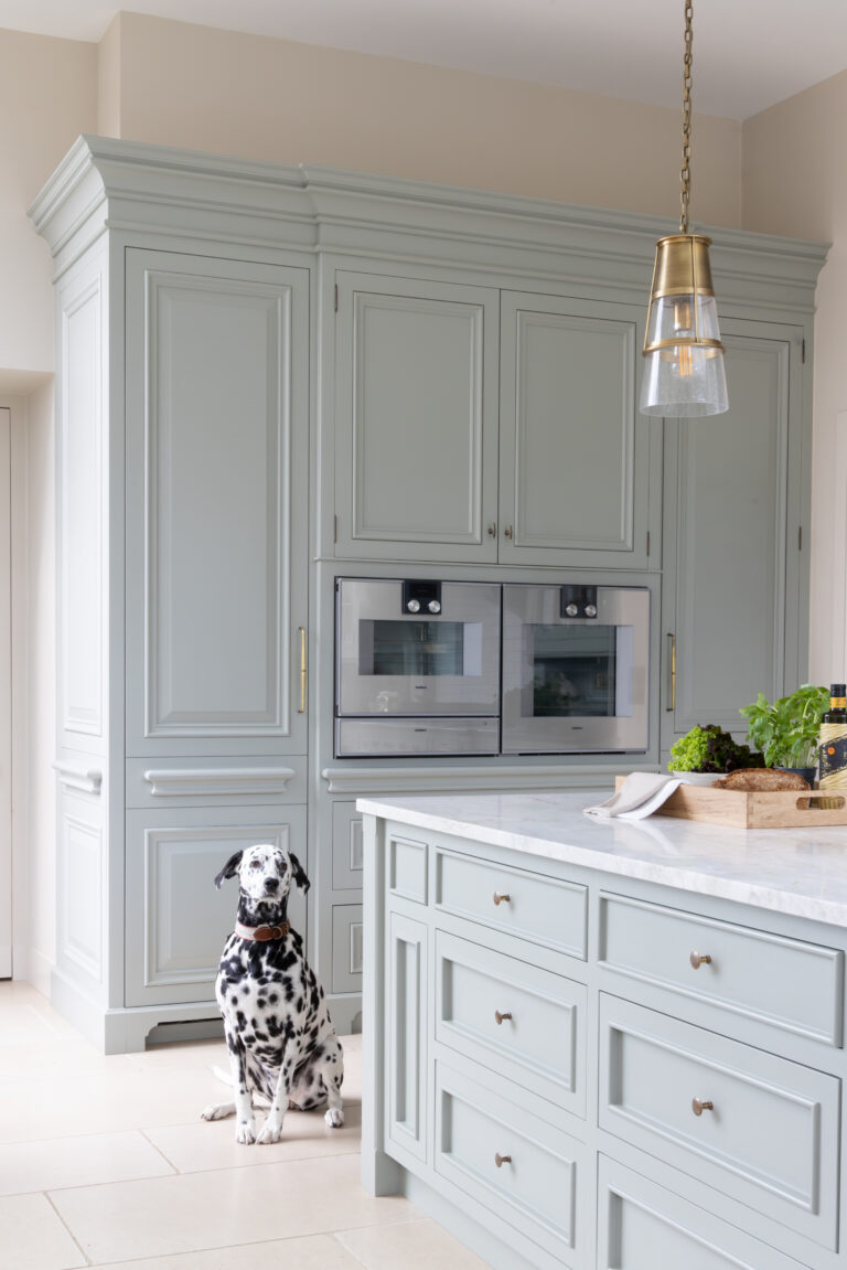 Sage Green kitchen with integrated ovens, brass pendant light and stone-topped island, a Dalmatian sitting nearby