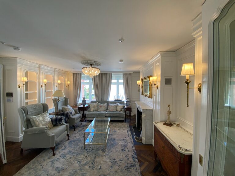 Sitting room with panelled bookshelves, armchairs and sofa, glass coffee table, and a stone fireplace surround