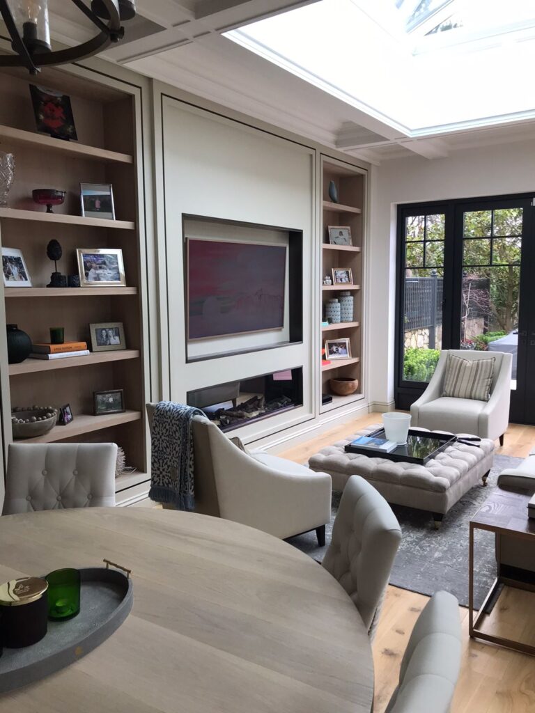 Living room with fitted shelving either side of a built-in fireplace, armchairs, an ottoman and a skylight above