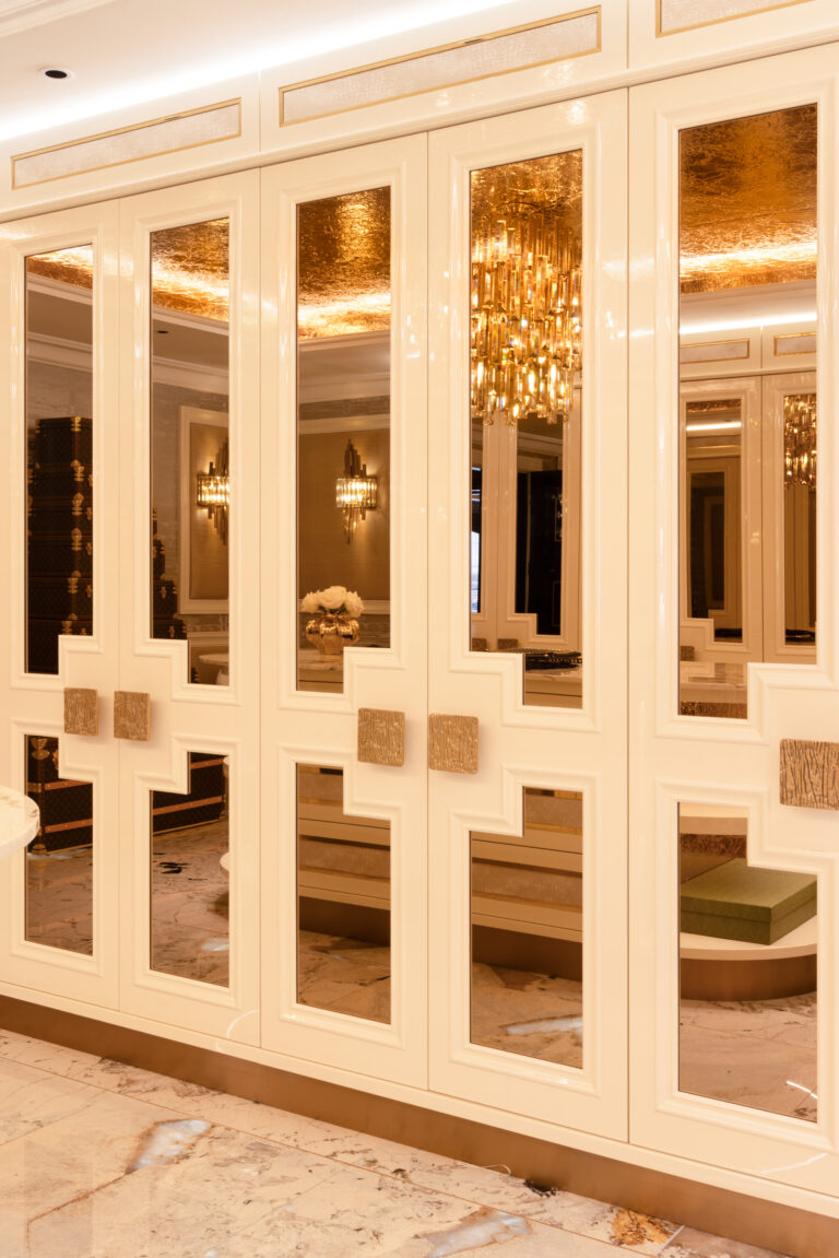 Dressing room wardrobe with mirrored panel doors, gold handles and a crystal chandelier reflected within