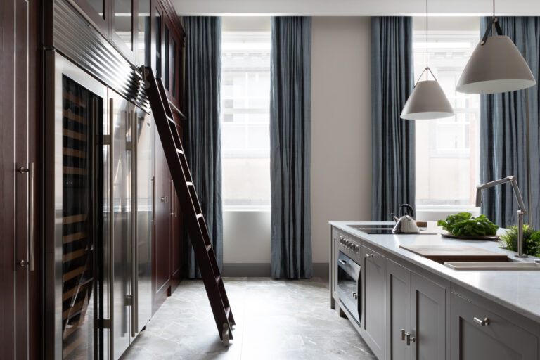 Kitchen with cherry wood cabinetry, a sliding library ladder, built-in oven and island beneath tall curtained windows