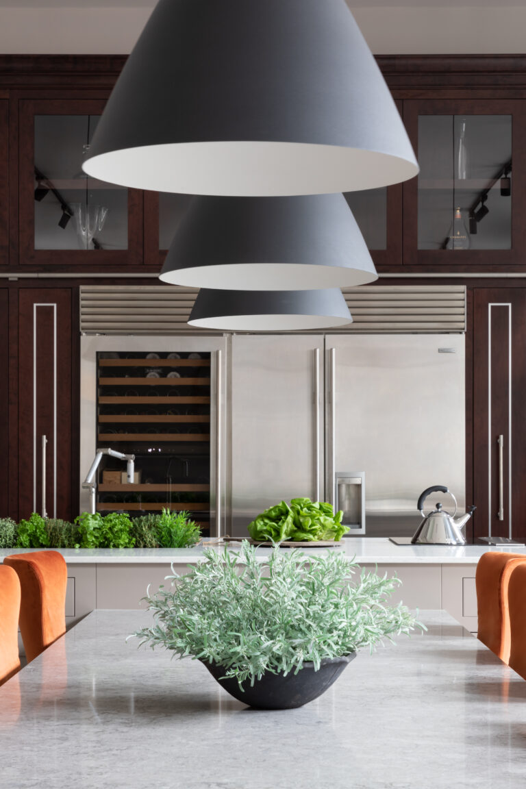 Dark cone pendant lights hang over a stone island with fresh herbs, facing integrated fridge and wine fridge cabinetry