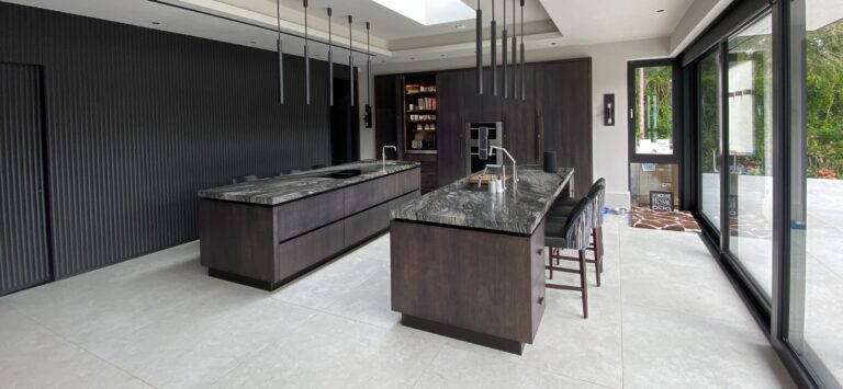 Open-plan kitchen with two dark wood islands, veined stone worktops, bar stools and fluted feature wall panelling