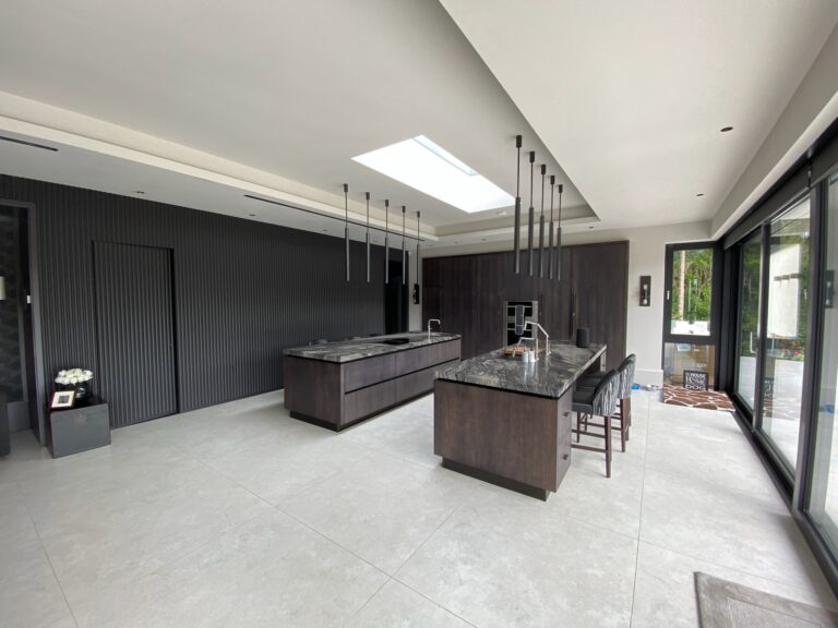 Open-plan kitchen with two dark wood islands, stone worktops, bar stools, ribbed wall panelling and a large skylight