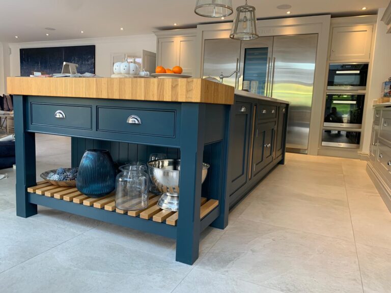 Kitchen island with blue painted cabinetry, wooden worktop, open slatted shelf, and integrated stainless steel appliances nearby