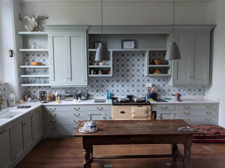 Kitchen with painted cabinetry, patterned tiled splashback, cream range cooker and a wooden table centred in the room