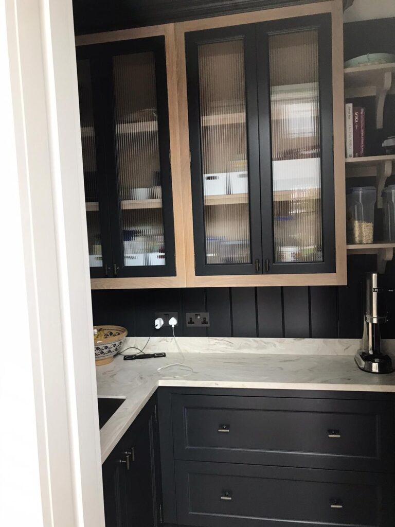 Pantry with dark cabinetry, fluted glass-fronted wall units, open shelving and a marbled worktop