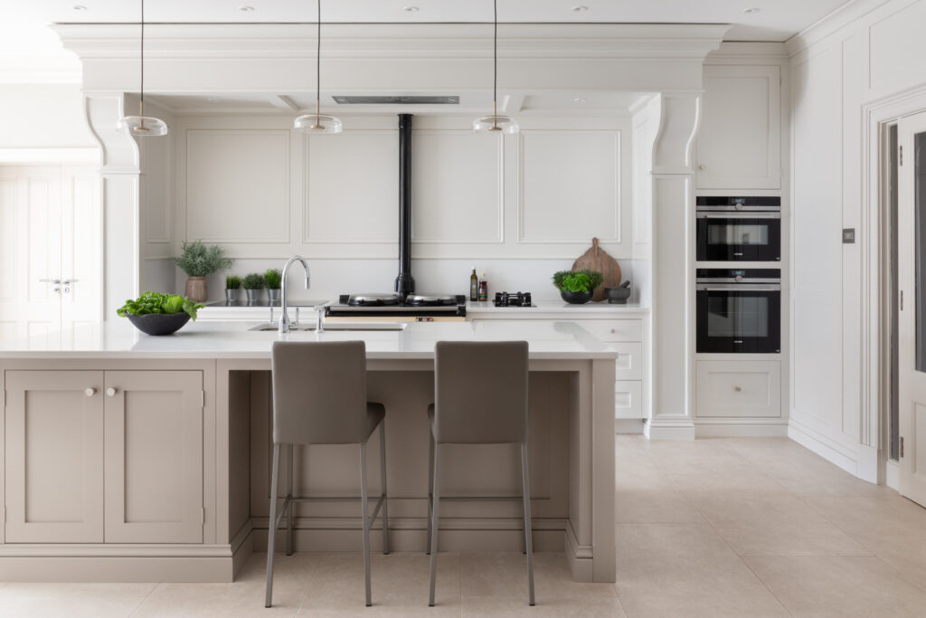 Kitchen island with bar stools facing an Aga with classic mantel detail and built-in double ovens beyond