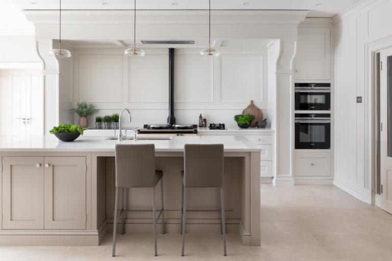 Kitchen island with bar stools facing an Aga with classic mantel detail and built-in double ovens beyond