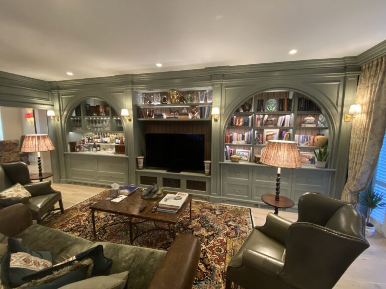 Sitting room with fitted sage-green bookcase units, arched display alcoves, integrated television and drinks cabinet