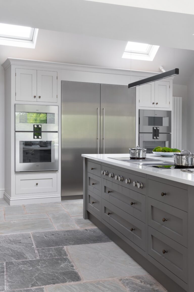 Grey island with induction hob sits beside white cabinetry, integrated ovens and a tall stainless fridge freezer