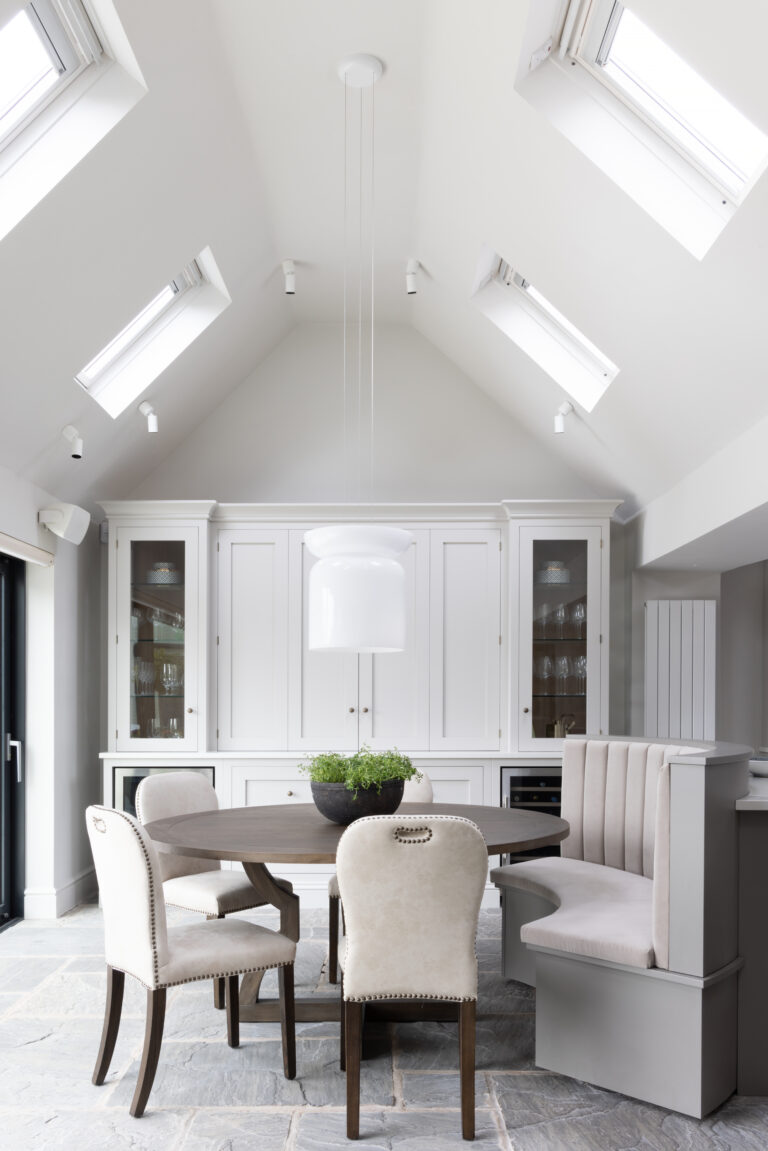 Vaulted ceiling dining area with round table, upholstered chairs, banquette seat and glazed display cabinets