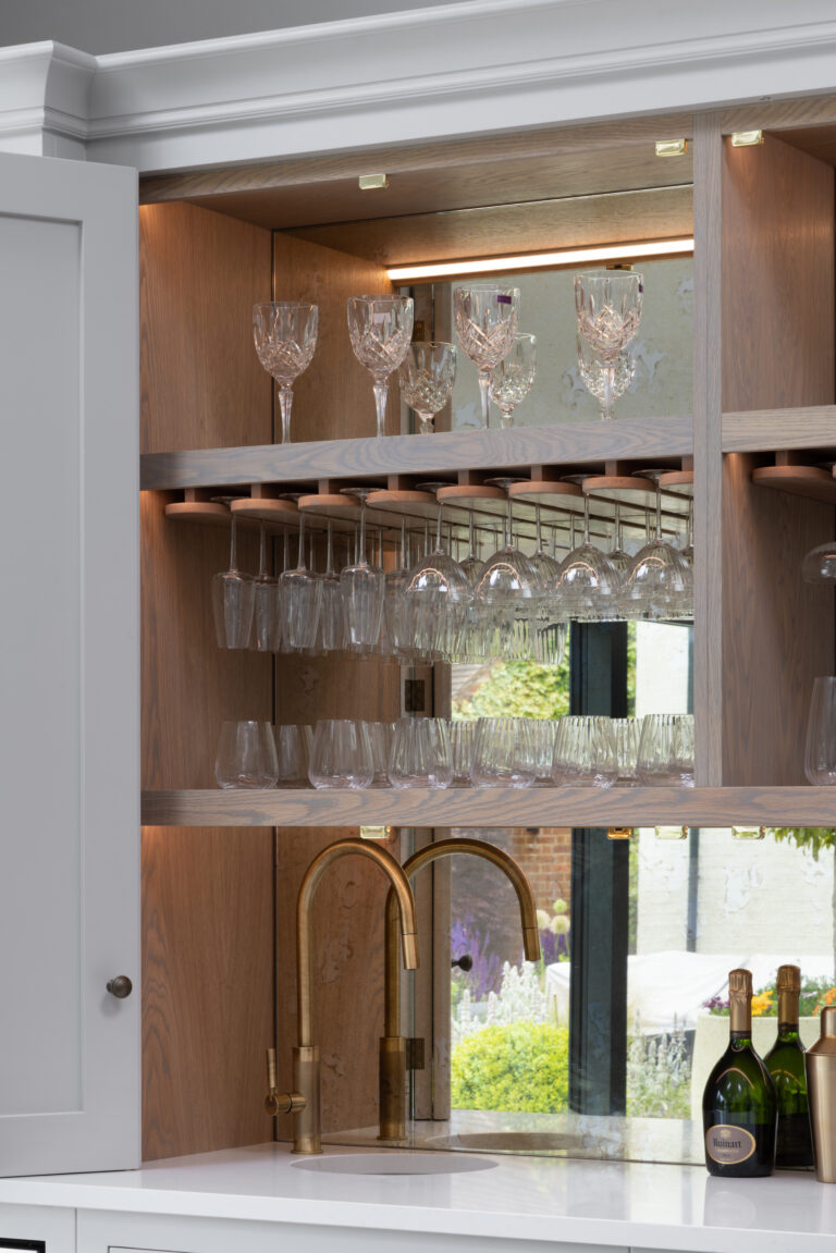 Bespoke home bar with mirrored splashback, brass tap, hanging glass racks and open shelving for glassware and bottles