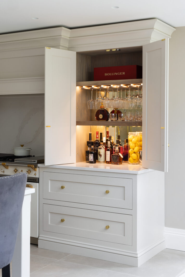 Shaker-style twin doors open to reveal a stained oak interior with glass racks, spirit bottles and brass fittings