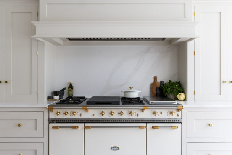 Lacanche range cooker with brass fittings sits beneath a panelled extractor hood and marbled splashback
