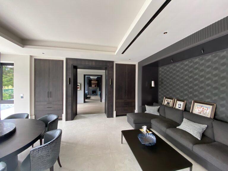Living room with a dark corner sofa, black coffee table, built-in wardrobes and a doorway leading to another room