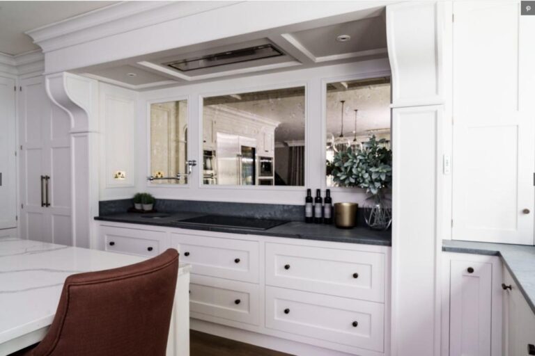Kitchen with white cabinetry, dark worktop, antiqued mirror splashback and an integrated induction hob beneath an extractor