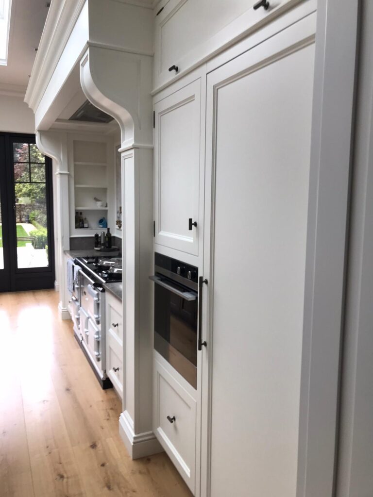 A bespoke kitchen with white panelled cabinetry, built-in oven, and a range cooker beneath an ornate extractor canopy