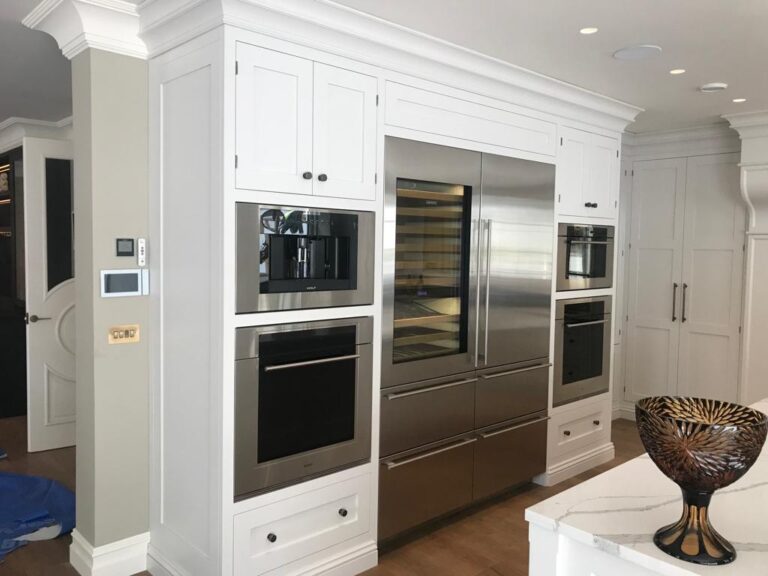 White painted kitchen cabinetry with integrated built-in ovens, coffee machine and a stainless steel glass-door fridge freezer